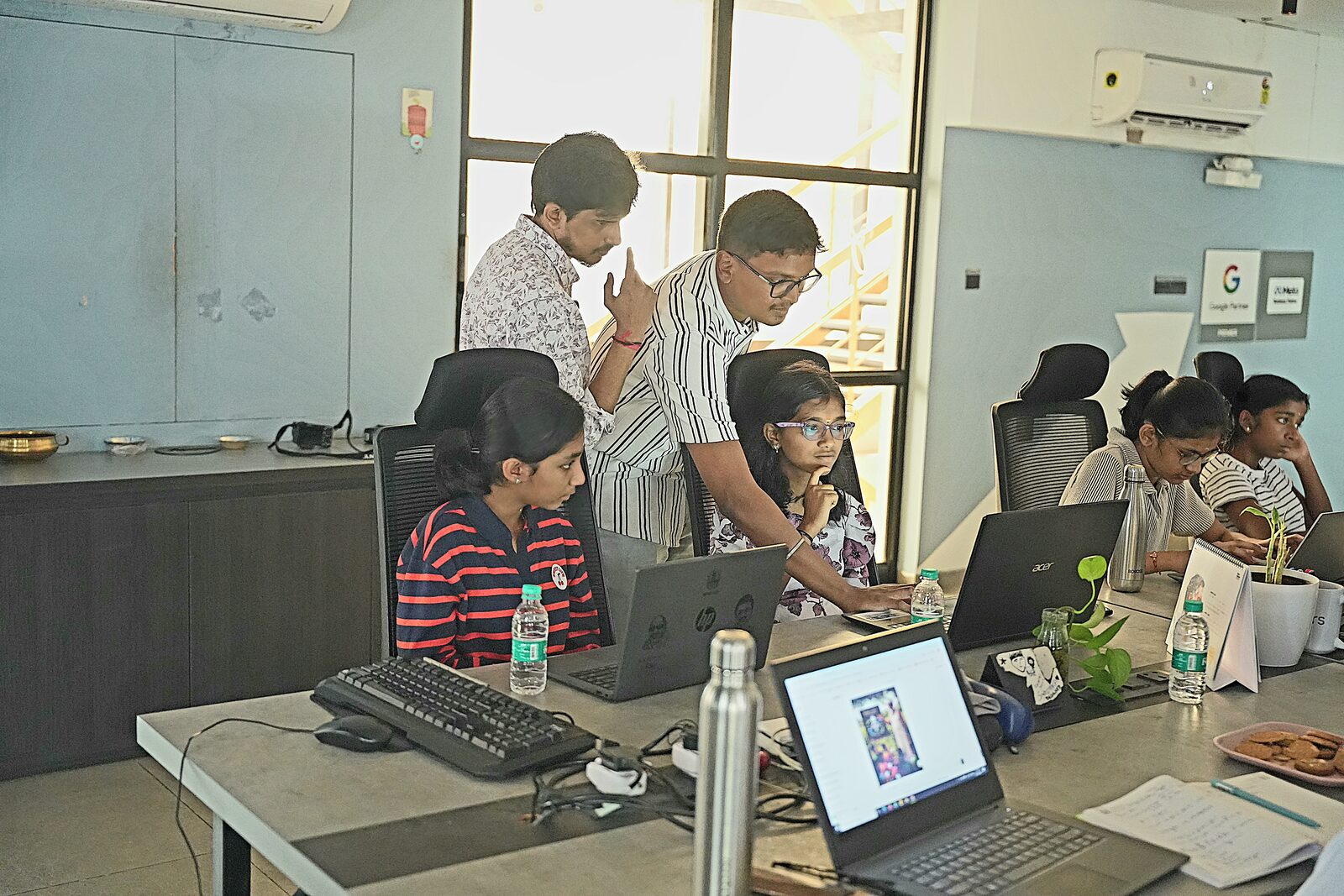 Rewire instructors guiding a group of students as they build AI projects on their laptops